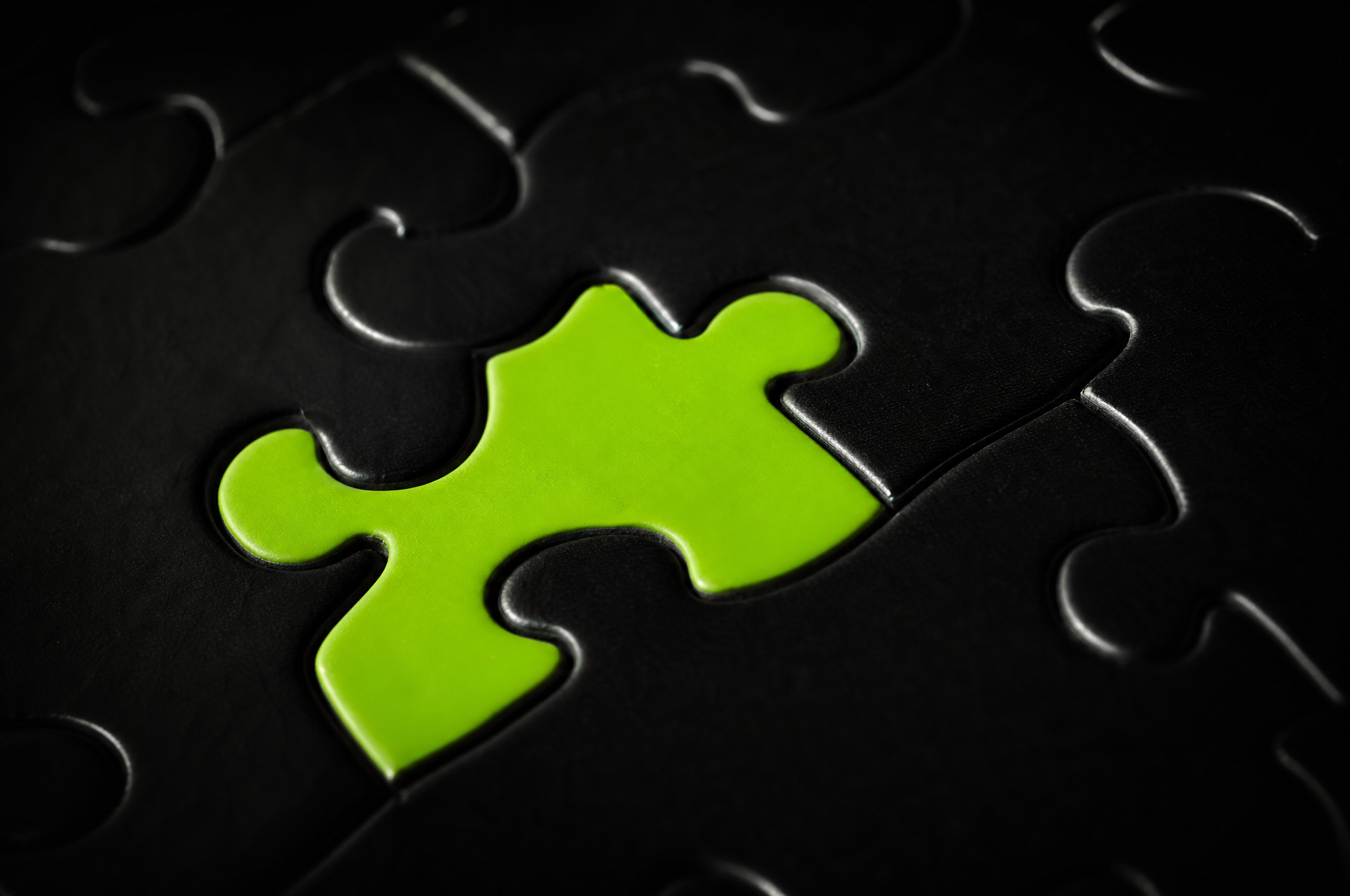 Primo piano su un singolo pezzo di puzzle verde lime che si incastra nella superficie nera
